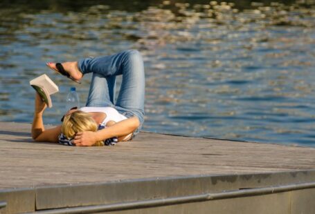 Downtime - woman in white tank top and gray pants lying on brown wooden dock during daytime