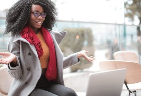 Video Content - Happy excited African American female laughing and gesticulating while having video calling on laptop and sitting at modern cafe