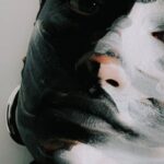 Color Psychology - Serious woman with face painted in black and white colors in black sweater and earrings looking at camera against white background