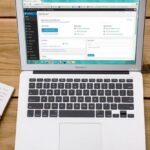 CMS - Turned-on Macbook Air Beside Black Iphone 4, Cup of Tea, and Notebook on Brown Wooden Surface