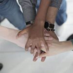 Continuous Integration - Crop from above of faceless multiracial friends in casual clothes uniting hands after coming to agreement while standing on light grey ceramic floor