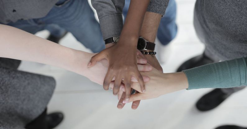 Continuous Integration - Crop from above of faceless multiracial friends in casual clothes uniting hands after coming to agreement while standing on light grey ceramic floor