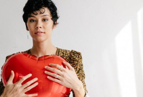 Form Friction - Serious female with red heart shaped balloon for Saint Valentine day standing against white wall