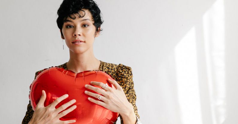 Form Friction - Serious female with red heart shaped balloon for Saint Valentine day standing against white wall